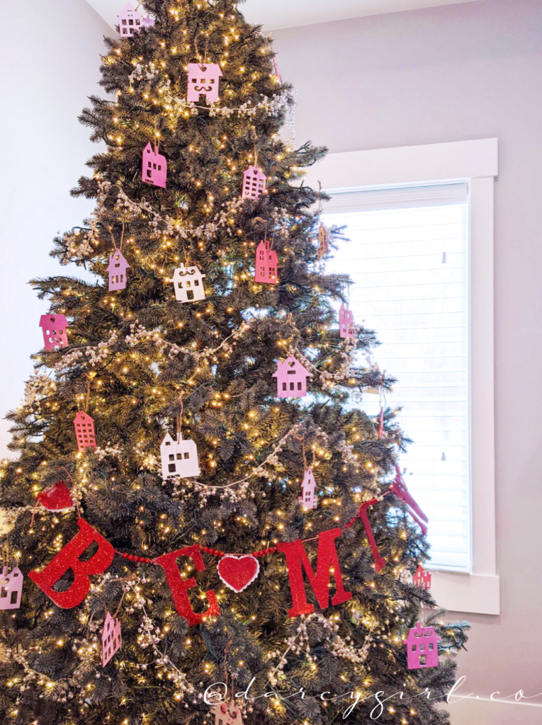 Christmas tree with pink and purple painted house ornaments and a garland that says, Be Mine.  