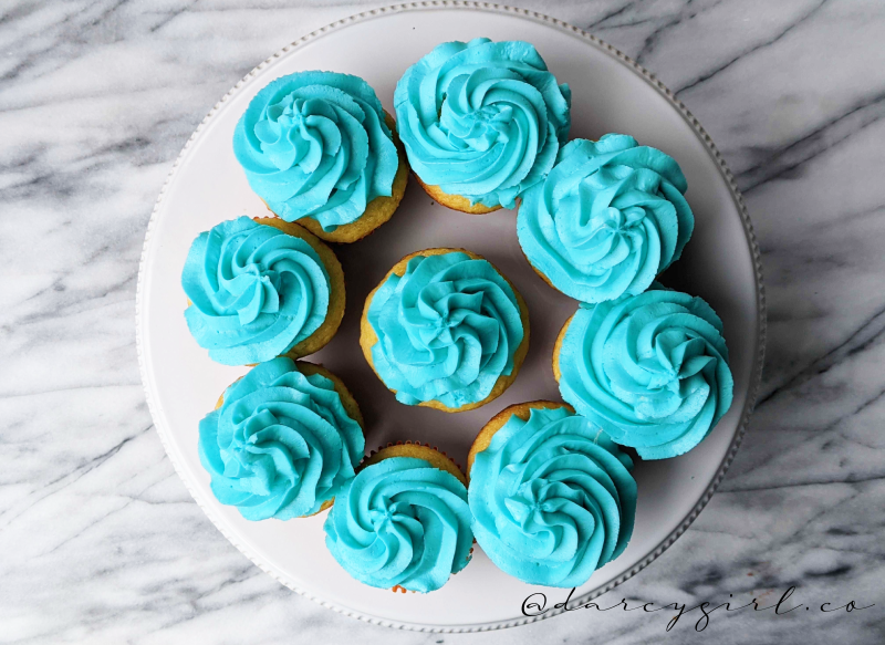 A plate of cupcakes with blue frosting.