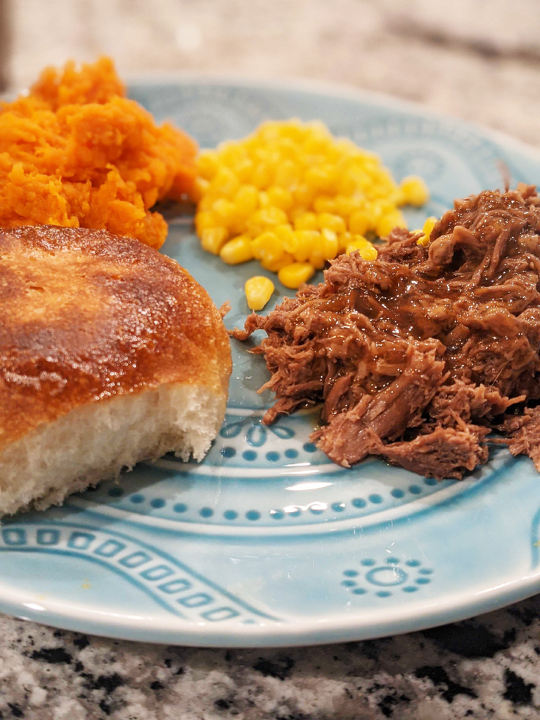 plate with beef, a roll, corn and yams.