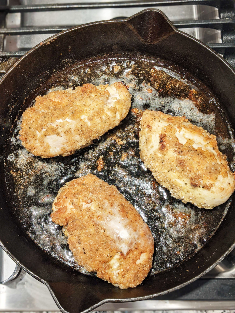 Three pieces of chicken being fried in a cast-iron skillet. 